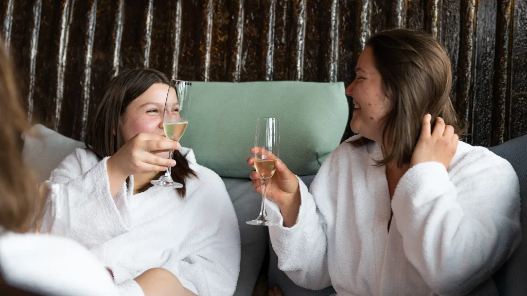 zwei Frauen in Bademänteln prosten sich mit gefüllten Sektgläsern zu