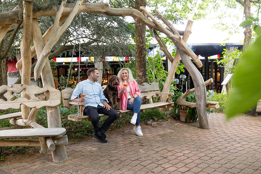 Ein Mann und eine Frau sitzen zusammen mit einem Hund auf einer Holzschaukel