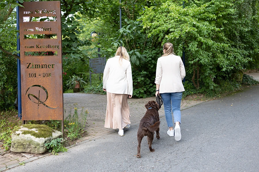 Zwei Frauen gehen mit einem Hund einen Weg entlang