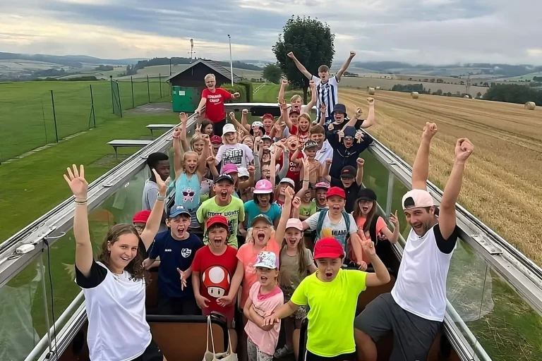 Eine Gruppe Kinder im oberen Deck eines Cabrio-Busses, die in die Kamera schauen und die Hände heben
